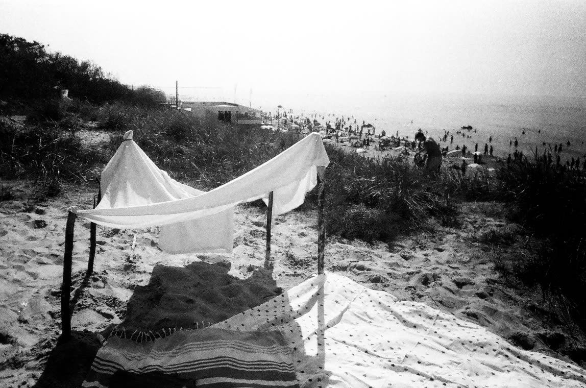 Sheet strung between poles on a crowded beach, 35mm