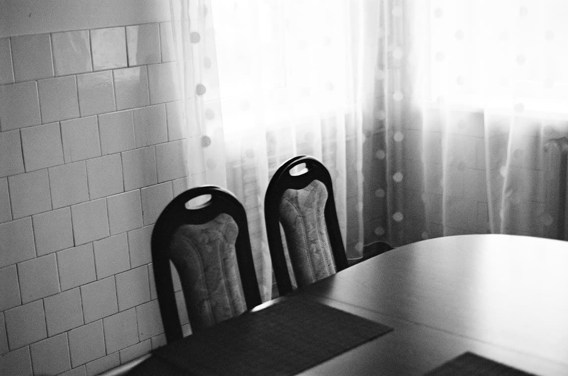 Two chairs at a table by a curtained window, 35mm