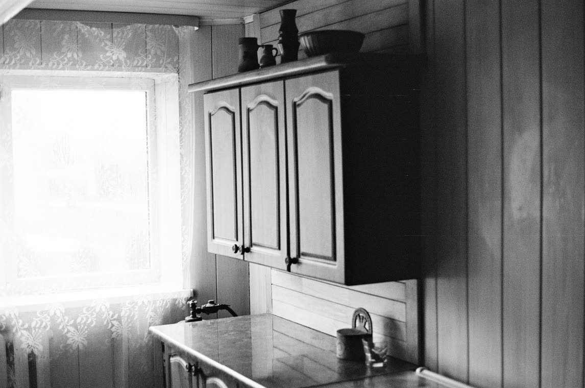Kitchen cabinets beside a lace-curtained window, 35mm
